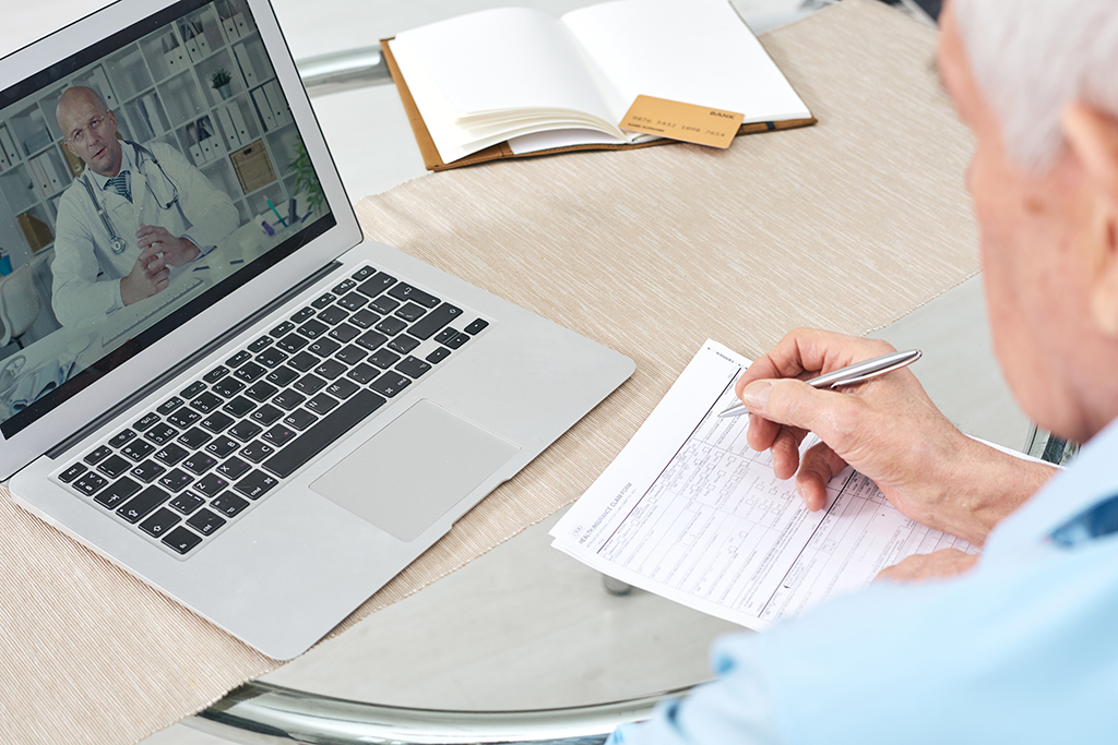Retired man watching online video of medical consultation on laptop display